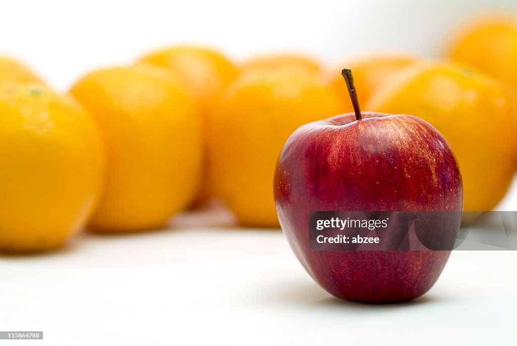 Lone apple standing in front of several blurred oranges