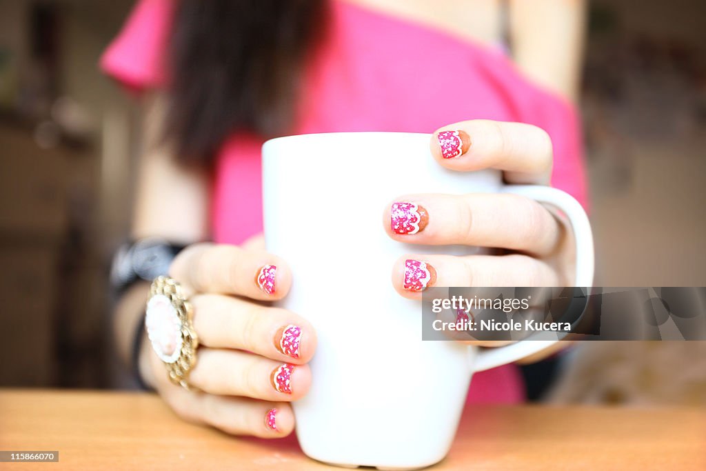 Girl holding coffee mug with cupcake nail design