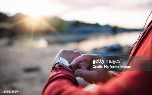 a midsection of sportsman runner with smart watch standing outdoors on beach. - checking sports fotografías e imágenes de stock