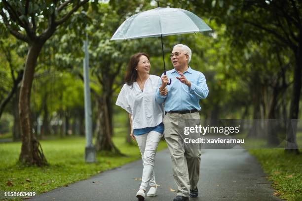 senior asian couple walking in taipei park with umbrella - sharing umbrella stock pictures, royalty-free photos & images