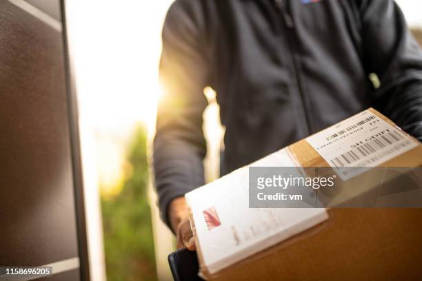 corriere che tiene scatola di cartone per la consegna - contenitore foto e immagini stock
