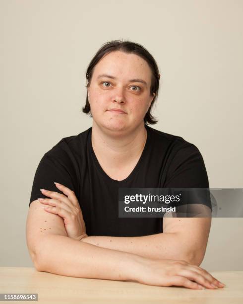studio portrait of a 35 year old woman in a black t-shirt sitting at a table on a beige background - black t shirt on table stock pictures, royalty-free photos & images