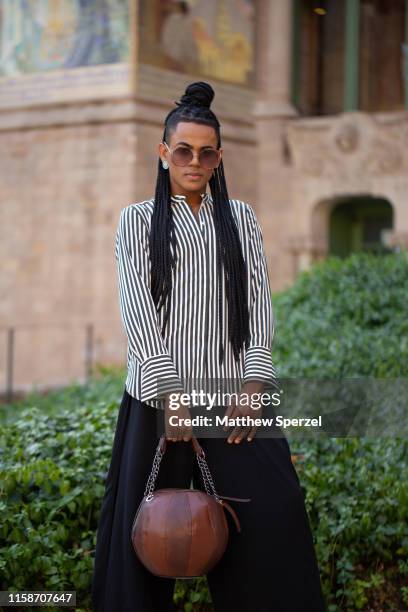 Guest is seen on the street attending 080 Barcelona Fashion Week wearing black/white striped shirt, brown leather bag, and wide black pants and on...