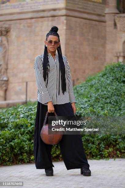 Guest is seen on the street attending 080 Barcelona Fashion Week wearing black/white striped shirt, brown leather bag, and wide black pants and on...