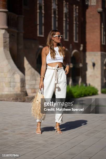 Guest is seen on the street attending 080 Barcelona Fashion Week wearing white crop top, white high-waist pants and a Jacquemus straw bag on June 27,...