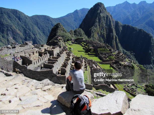 woman sitting on a rock sighting machu picchu from above - berg huayna picchu stock-fotos und bilder