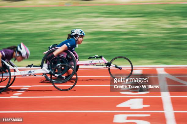young female wheelchair racers crossing the finish line at a track and field event - wheelchair athlete stock pictures, royalty-free photos & images