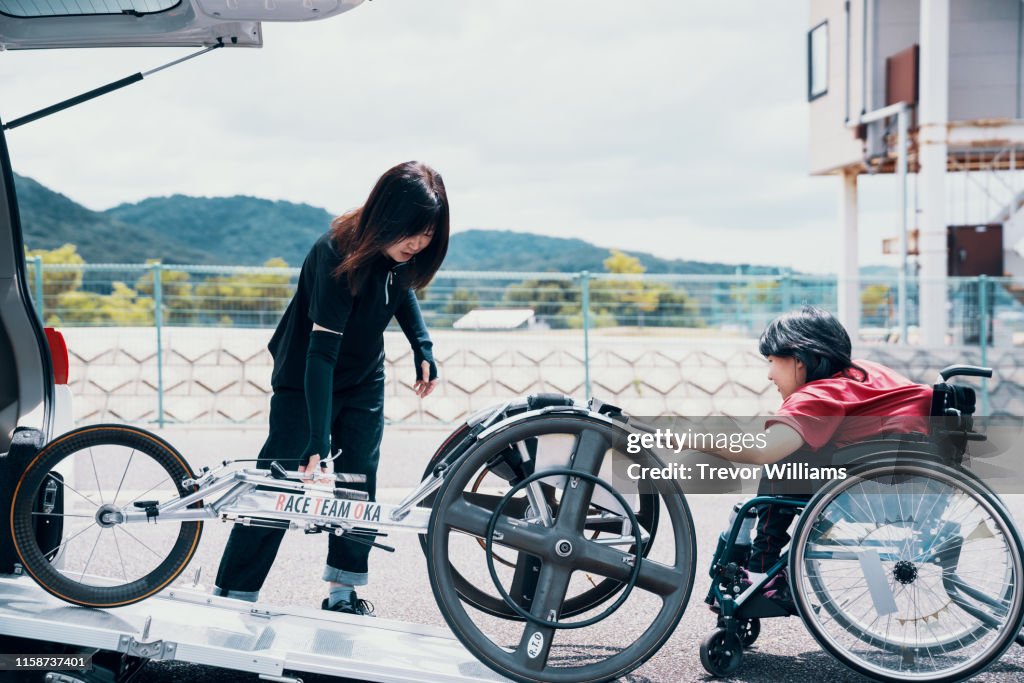 Young female wheelchair racerunloading her racing wheelchair from a car