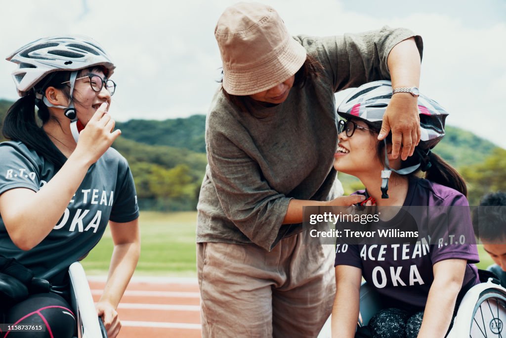 Young female wheelchair racers prepare for a competition with the support of their parent or coach