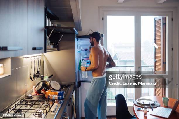 mid adult man removing bottled water from fridge - semi dress - fotografias e filmes do acervo