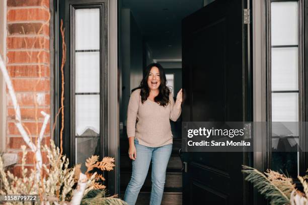 mid adult woman opening house front door, portrait - voordeur stockfoto's en -beelden