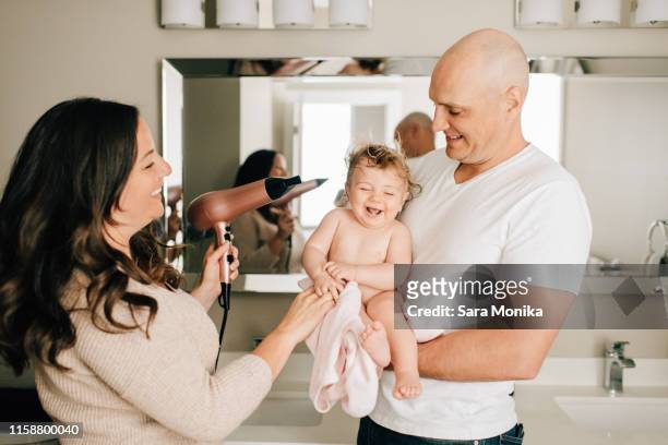 mother and father drying baby daughter's hair in bathroom - blow drying hair stock-fotos und bilder