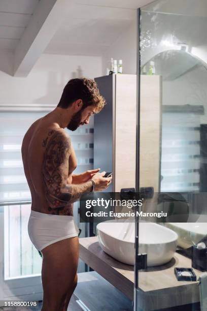 mid adult man with tattoos looking at smartphone at bathroom mirror - slip stock-fotos und bilder