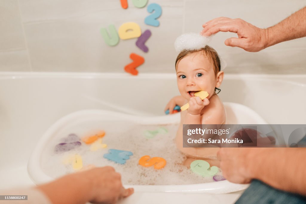 Mother and father putting bath suds on baby daughter's head, cropped