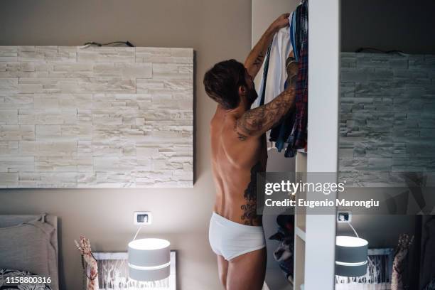 mid adult man with tattoos selecting shirt from wardrobe - slip stock-fotos und bilder