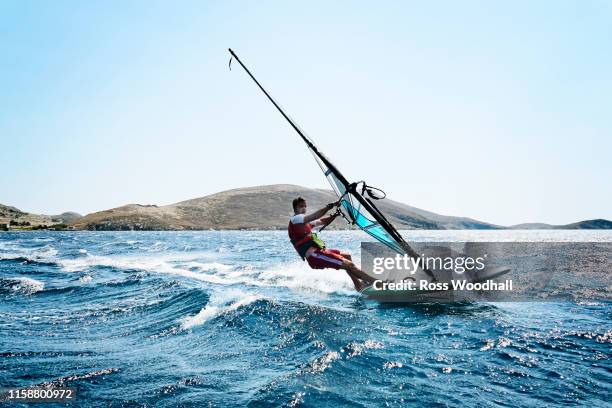 young man windsurfing ocean waves, side view, limnos, khios, greece - wind surfing stock pictures, royalty-free photos & images