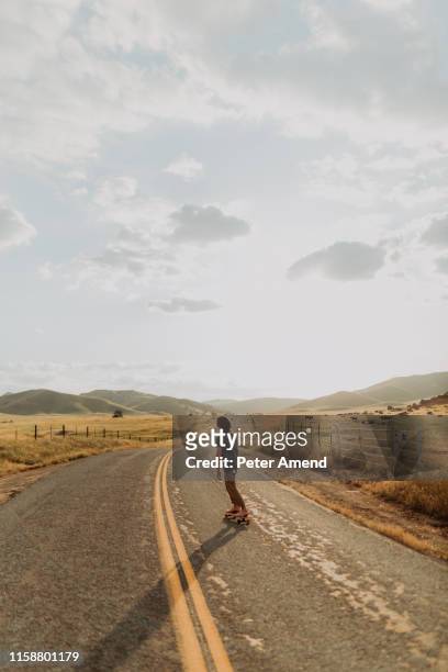 young barefoot male skateboarder skateboarding on rural road, rear view, exeter, california, usa - confidence male landscape stock-fotos und bilder