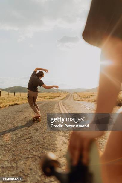 young barefoot male skateboarder skateboarding on rural road, girlfriend watching, exeter, california, usa - men's free skate imagens e fotografias de stock