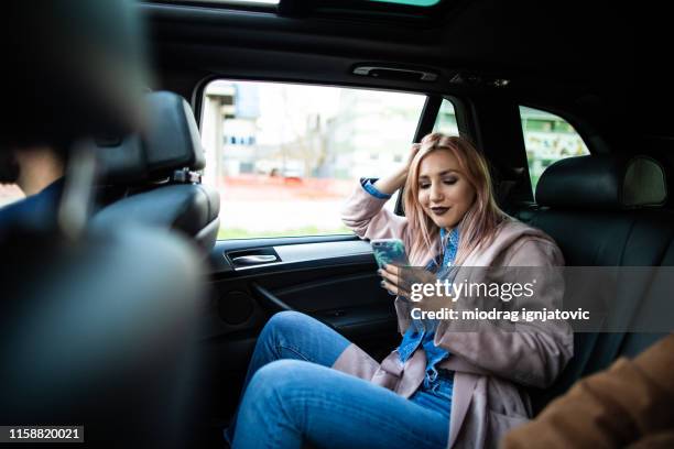 vrouw rijden op achterbank en het gebruik van smart phone - personenauto stockfoto's en -beelden