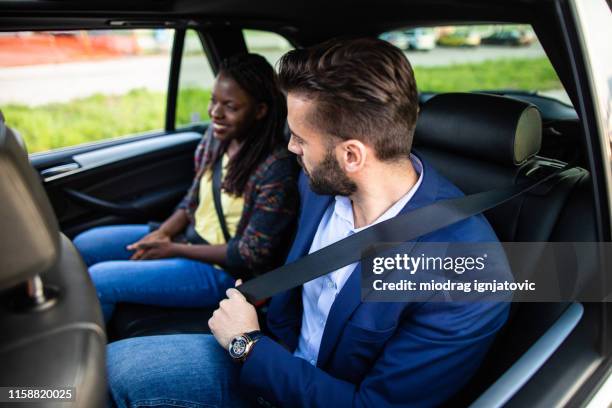 multi-ethnic couple on back seat in car - ethnic woman driving a car stock pictures, royalty-free photos & images