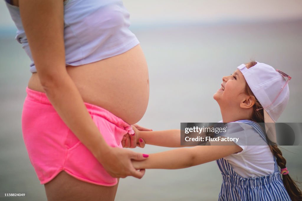 Excited child holding pregnant mother's hands on the beach
