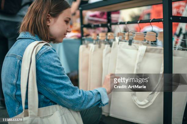 junges mädchen wählt umweltfreundliche wiederverwendbare baumwoll-einkaufstasche auf einem open-air-markt mit null-abfall-shopping-konzept - stoffbeutel stock-fotos und bilder