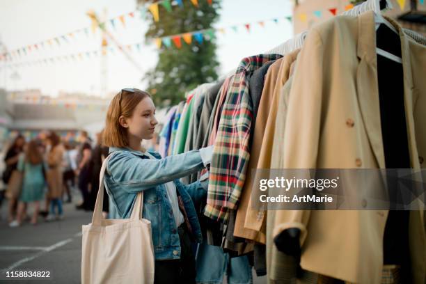 junges mädchen wählt kleidung in einem second-hand-markt im sommer, null-abfall-konzept - flohmarkt stock-fotos und bilder