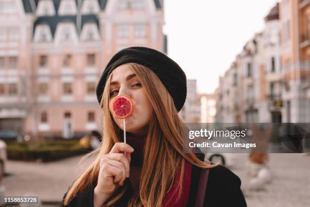 young woman kissing lollipop while standing on city street - candy lips stock pictures, royalty-free photos & images