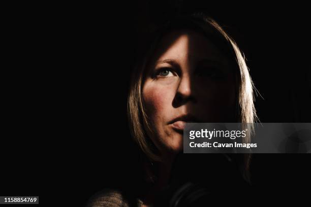 self portrait of a caucasian woman in her forties with shadow on face - schwache beleuchtung stock-fotos und bilder