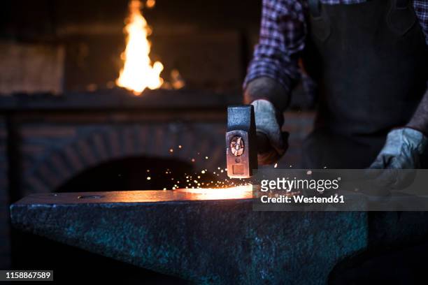 close-up of blacksmith working with hammer at anvil in his workshop - schmied stock-fotos und bilder