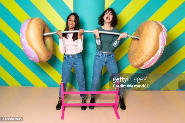 two happy young women at an indoor theme park having fun with oversized donuts - picking up food stock pictures, royalty-free photos & images