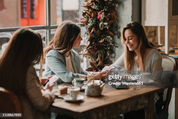 three happy young women with cell phone meeting in a cafe - female friends stock pictures, royalty-free photos & images