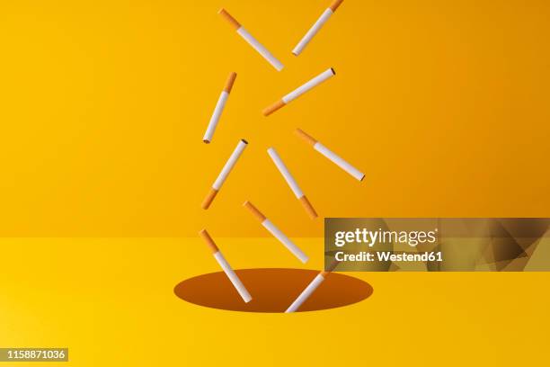 cigarettes falling into a hole in yellow background - cigarette stock illustrations