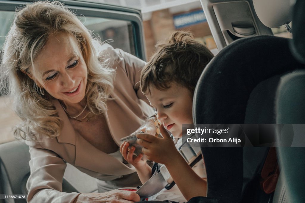 Grandmother putting boy in the car seat