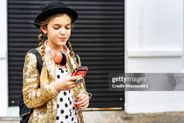 portrait of girl with headphones wearing hat and golden sequin jacket looking at cell phone - gold jacket stock pictures, royalty-free photos & images