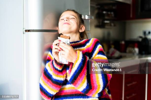 girl in striped pullover in kitchen at home eating chocolate - chocolate closed eyes stock-fotos und bilder