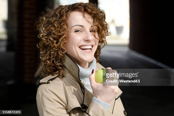 portrait of laughing woman with curly hair with green apple - eat apple stock pictures, royalty-free photos & images