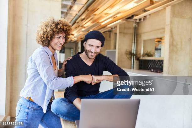 happy man and woman with laptop fist bumping in modern office - casual woman business stock-fotos und bilder