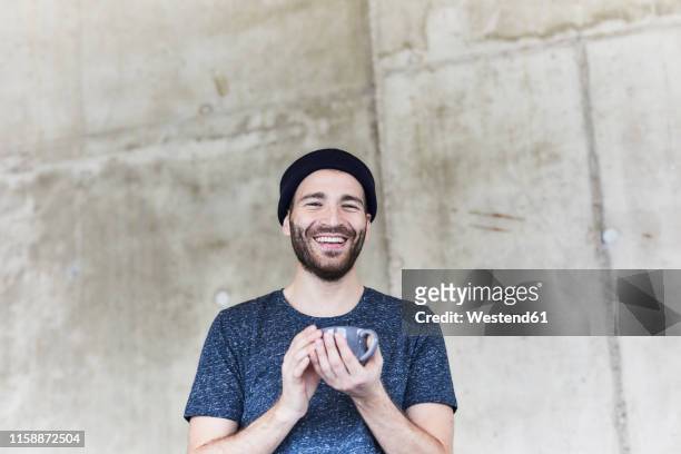 happy young man holding cup at concrete wall - appreciation stock-fotos und bilder