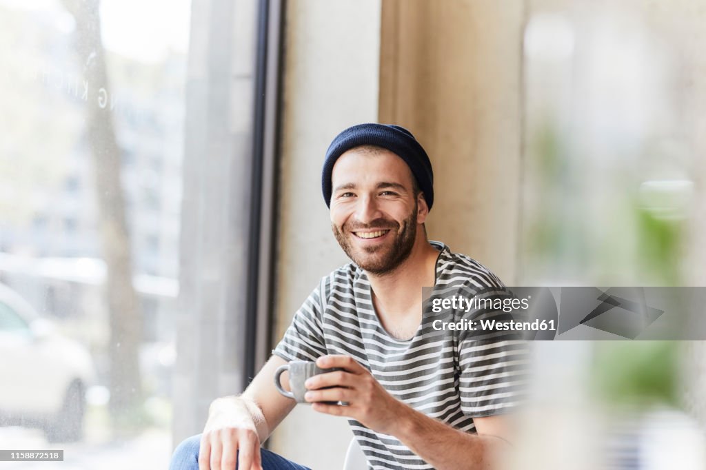 Portrait of smiling young man holding coffee cup at the window