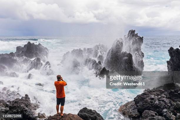 usa, hawaii, big island, laupahoehoe beach park,man taking pictures of breaking surf at the rocky coast - littoral rocheux photos et images de collection