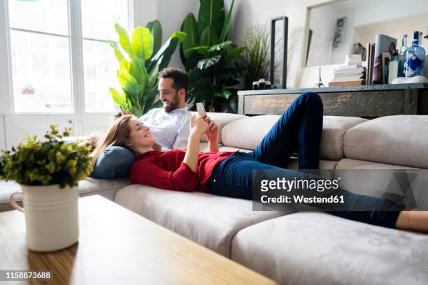 couple lying on couch, using heir smartphones - couple smartphone stockfoto's en -beelden