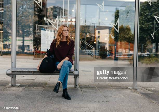 young woman sitting at bus stop with bag - bushaltestelle stock-fotos und bilder