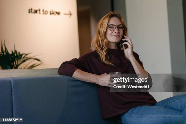 smiling young woman sitting on couch talking on cell phone - businesswoman couch fotografías e imágenes de stock