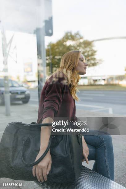 young woman sitting at bus stop with bag - sporttasche stock-fotos und bilder