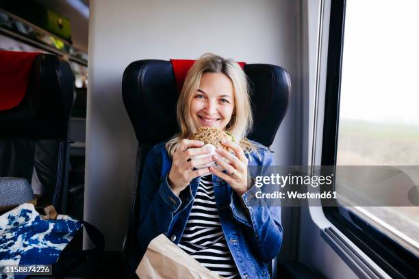 portrait of smiling blond woman travelling by train having a snack - snacking on the go stock-fotos und bilder