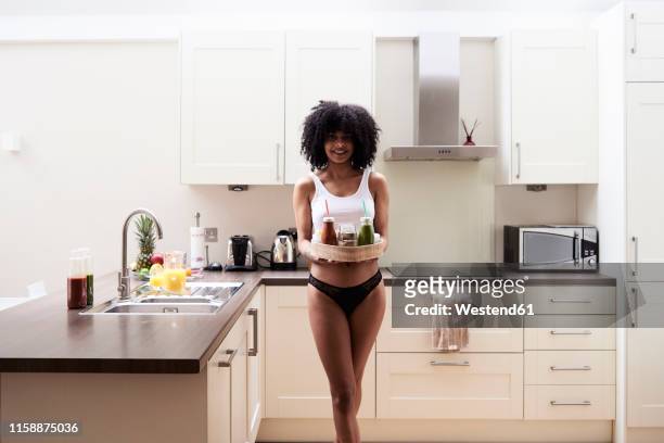 smiling young woman carrying healthy breakfast tray in kitchen - women in slips stock-fotos und bilder