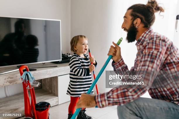 father and little daughter having fun together while cleaning the living room - chores stock-fotos und bilder