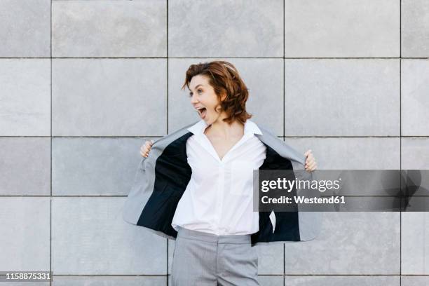 portrait of a screaming young businesswoman in front of wall with gray tiles, opening her jacket - coat stock-fotos und bilder