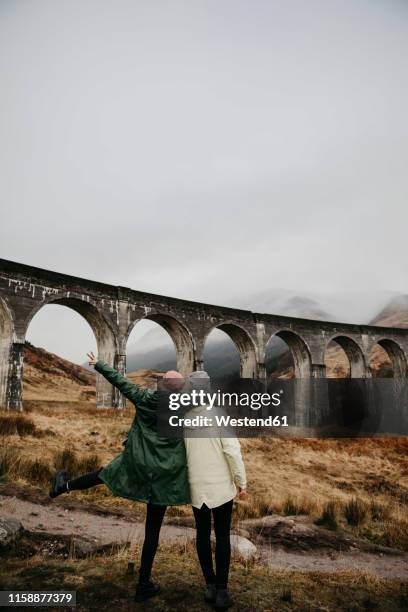 uk, scotland, highland, glenfinnan viaduct, rear view of female friends looking at view - glenfinnan viaduct stockfoto's en -beelden